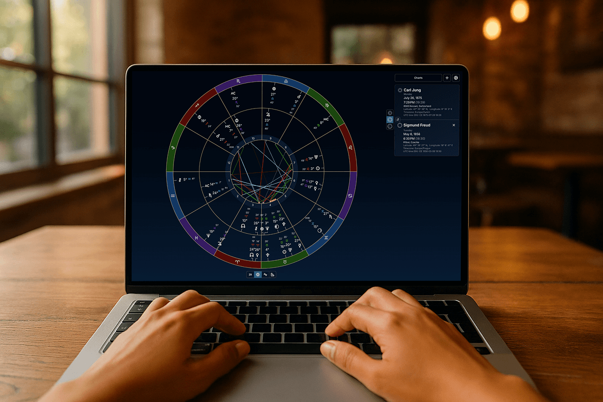 First person perspective of hands typing on a laptop displaying the Astrotheoros app with a synastry chart. The setting is a cozy cafe with warm lighting.